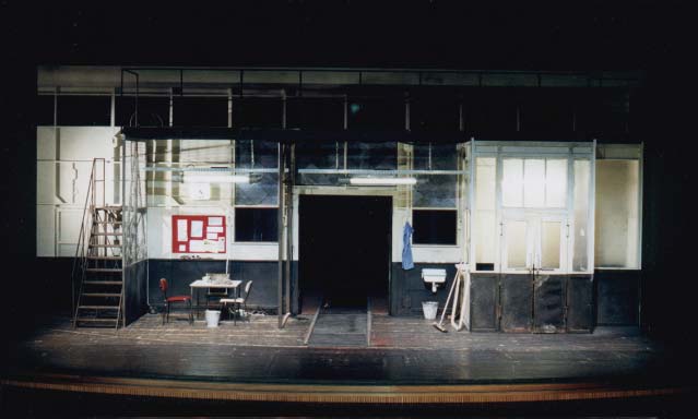 DER GETEILTE HIMMEL Volksbühne Berlin, Bühne Alissa Kolbusch. Eine alte leere blau- beige DDR- Fabrik mit einem Kontor rechts , einem Tisch mit Stühlen und einer Treppe links