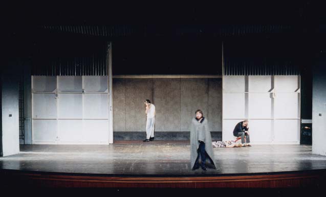 DER GETEILTE HIMMEL Volksbühne Berlin, Bühne Alissa Kolbusch. 2 Schauspieler stehen vor einem geöffneten Werks- Tor , einer sitzt davor auf dem Boden.