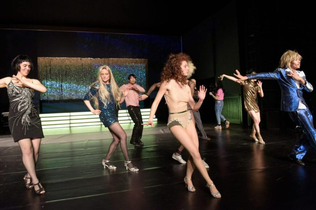 DER PALAST Volksbühne Berlin, Bühnenbild: Alissa Kolbusch. Acht Darsteller*innen tanzen vor einer Showtreppe und einem silbernen Glitzervorhang.