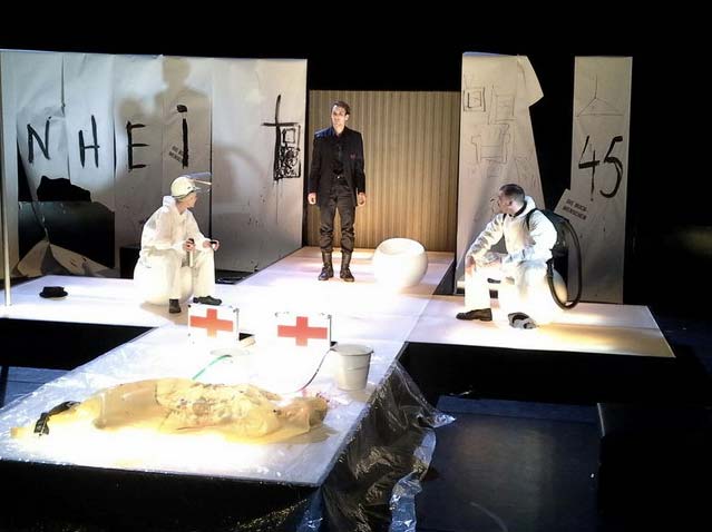 FAHRENHEIT 541 Hans- Otto- Theater Potsdam, Bühnenbild: Alissa Kolbusch. Auf einem weißen Kreuz aus Stegen mit 3 Sitzkugeln darauf sitzen und stehen drei Darsteller. 2 Rotkreuz- Koffer vorne, hinten weiße Papierbahnen auf den schwarzen Wänden.