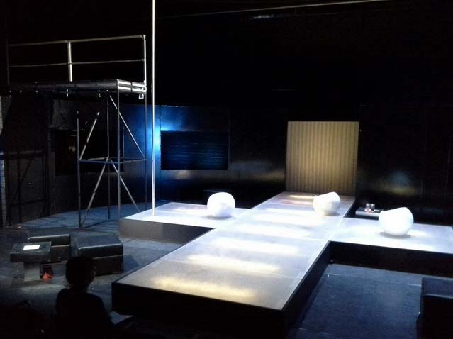 FAHRENHEIT 541 Hans- Otto- Theater Potsdam, Bühnenbild: Alissa Kolbusch. Ein weißes Kreuz aus Stegen mit 3 Sitzkugeln darauf, links ein hoher Steg , hinten schwarze Wände, vorne rechts und links Sitzwürfel.