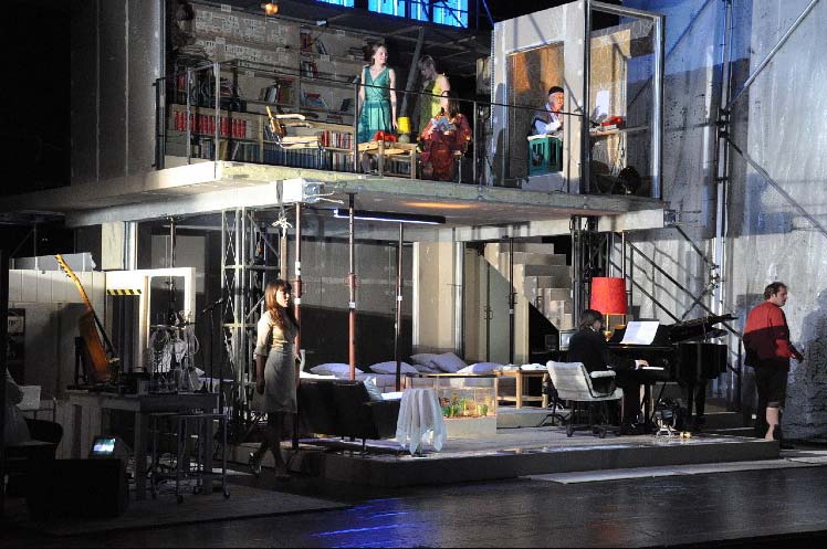 RHEINGOLD, Staatsschauspiel Dresden, Bühne und Kostüme Alissa Kolbusch. ein 2- stöckiges Rohbau- Haus, provisorisch eingerichtet, mit einer Treppe, Geländer und Möbeln. Unten ein Pianist am Flügel und 2 Darsteller, die singen, oben 2 Darstellerinnen und ein Mann in einer Tonkabine.