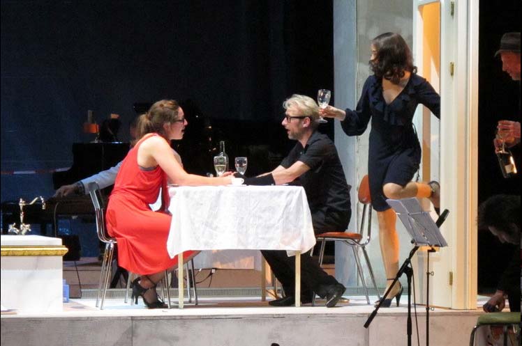 DIE KRÖNUNG DER POPPEA, Bühne und Kostüme: Alissa Kolbusch. Eine große weisse Wohnlandschaft, Nahaufnahme auf ein Podest, auf dem eine Badewanne und ein Esstisch stehen. Ein Paar sitzt am Esstisch und diskutiert, eine Frau kommt durch die Tür rein.