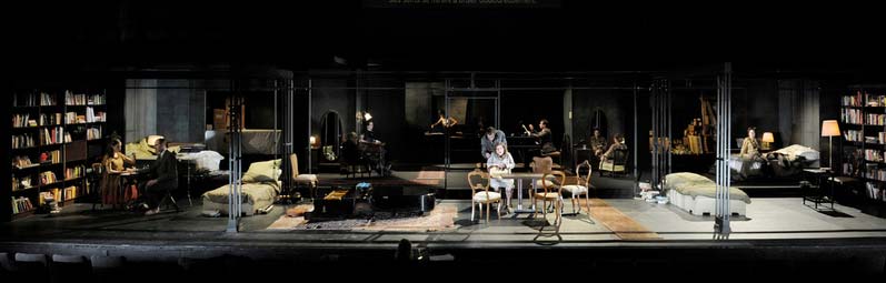DAS WOHLTEMPERIERTE KLAVIER, Schaubühne Berlin/MC93 Bobigny, Bühnenbild Alissa Kolbusch. Ein dunkles breites Wohnzimmer mit antiken Stühlen und einem Flügel der ohne Beine auf dem Teppich liegt. daneben gespiegelt jeweils rechts und links ein Bibliothekszimmer mit Bett, Stehlampe und Sessel. Dahinter 2 Räume mit Schmink- Kommode, in der Mitte dahinter ein Flur mit einem Bügelbrett. vereinzelt sitzen die Darsteller in jeweils einem der Räume .