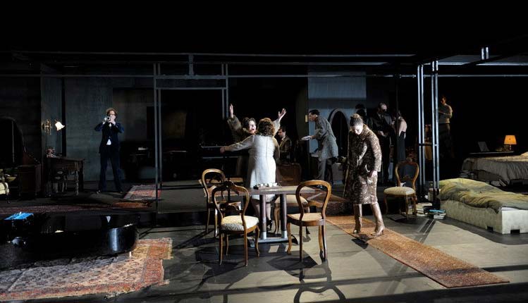 DAS WOHLTEMPERIERTE KLAVIER, Schaubühne Berlin/MC93 Bobigny, Bühnenbild Alissa Kolbusch. Ein dunkles breites Wohnzimmer mit antiken Stühlen und einem Flügel der ohne Beine auf dem Teppich liegt. Viele Menschen laufen wild gestikulierend herum.