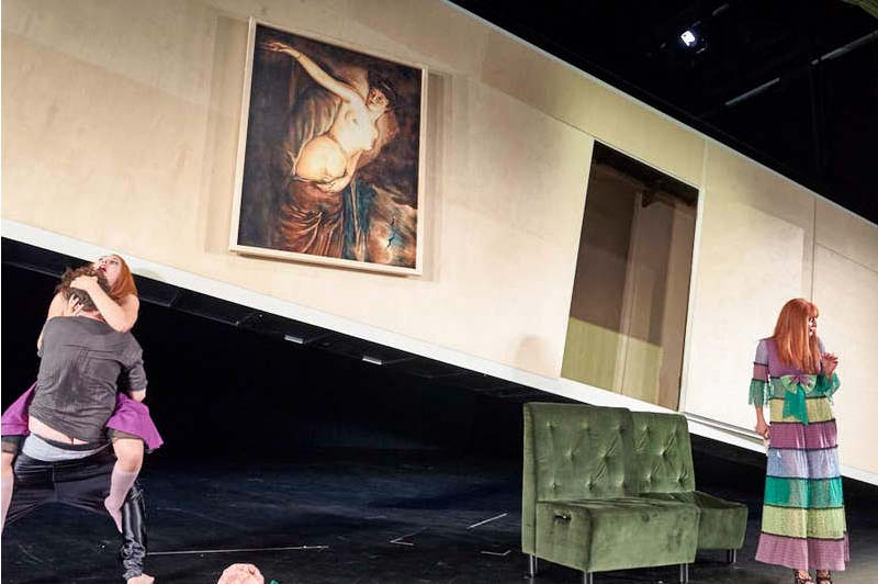 DER REVISOR Düsseldorfer Schauspielhaus, Bühne und Kostüme: Alissa Kolbusch. Vor der hängenden Wand kopuliert der Schauspieler mit der anderen Frau, während die Frau im bunten Kleid pikiert zur Seite schaut