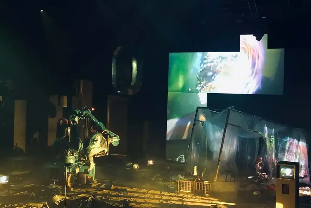 GROUND CONTROL Maxim Gorki Theater Berlin, Bühne: Alissa Kolbusch. Eine Darstellerin sitzt auf einem Roboter- Arm. Auf dem Boden und im Hintergrund eine zerfallene Landschaft mit Videoinstallation in grünem Licht.