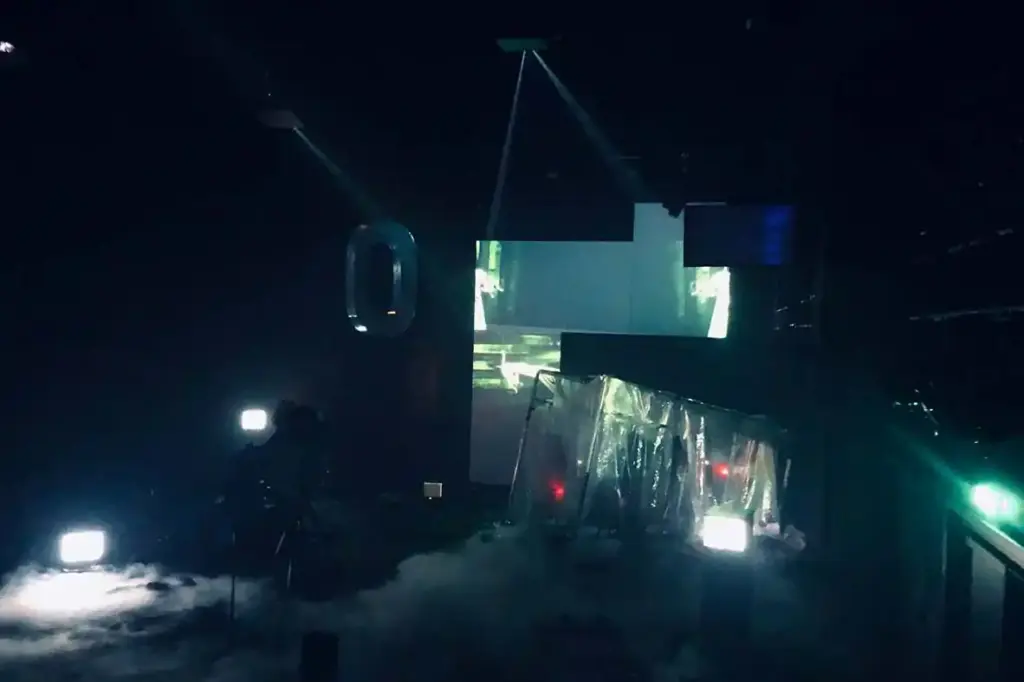 GROUND CONTROL Maxim Gorki Theater Berlin, Bühne: Alissa Kolbusch. Hinten rechts ein halb versunkener Glaskasten, auf dem Boden Nebel und im Hintergrund eine Videoinstallation in weiß-grünem Licht.