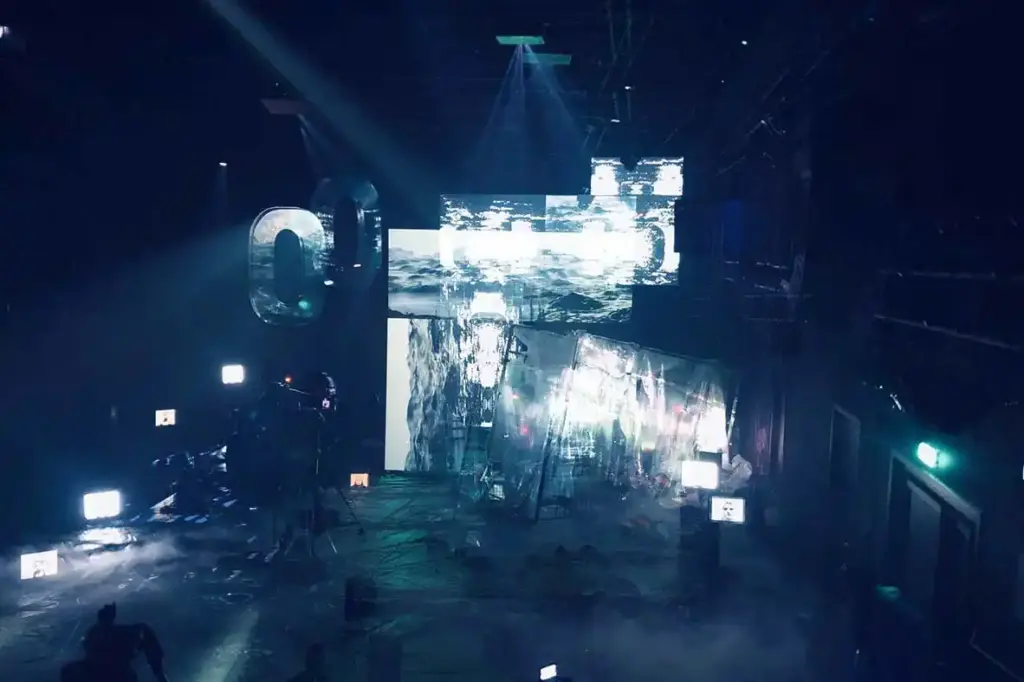 GROUND CONTROL Maxim Gorki Theater Berlin, Bühne: Alissa Kolbusch. Hinten rechts ein halb versunkener Glaskasten, auf dem Boden und im Hintergrund eine Videoinstallation in weißem Licht.