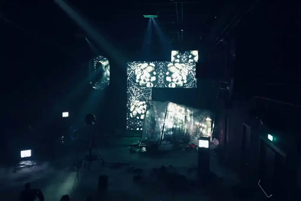 GROUND CONTROL Maxim Gorki Theater Berlin, Bühne: Alissa Kolbusch. Hinten rechts ein halb versunkener Glaskasten, auf dem Boden und im Hintergrund eine Videoinstallation in weißem Licht.