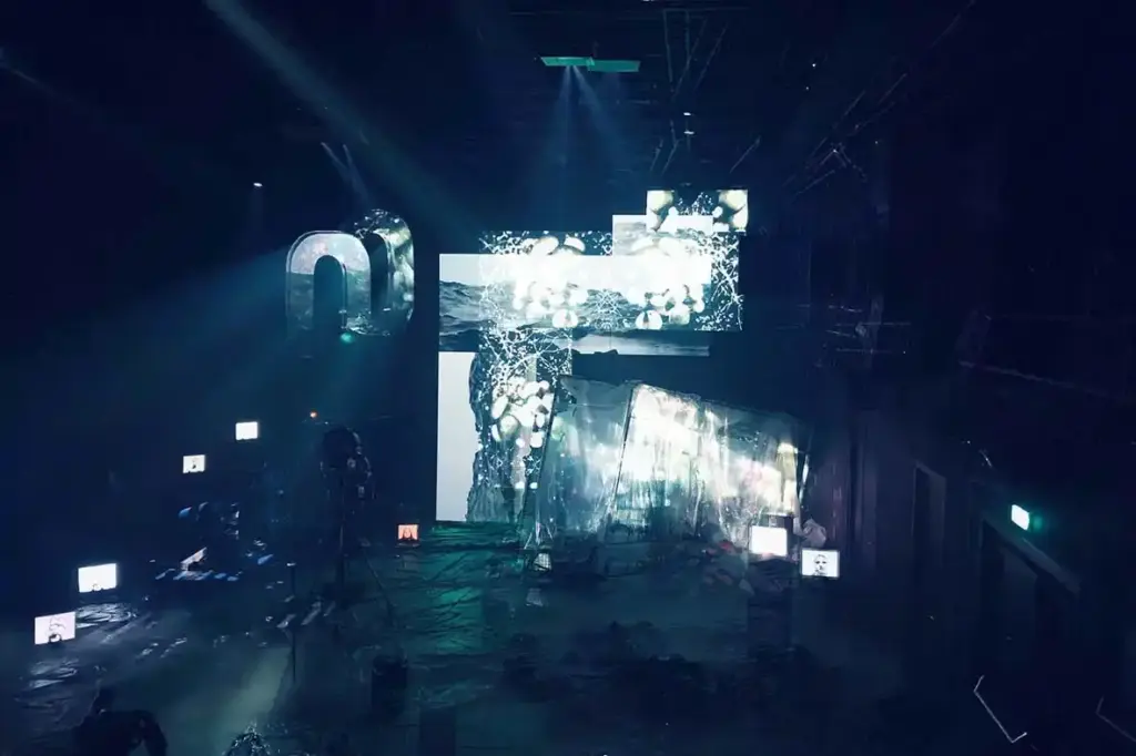 GROUND CONTROL Maxim Gorki Theater Berlin, Bühne: Alissa Kolbusch. Hinten rechts ein halb versunkener Glaskasten, auf dem Boden und im Hintergrund eine Videoinstallation in weißem Licht.